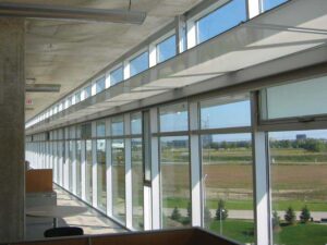 Viewed from the interior, a photograph of a light shelf within a window assembly in the horizontal position. The exterior louvres are in the same plane and partly visible. A rigging system raises and lowers the light shelves and the valence of the window coverings in response to late, low afternoon sun penetrating the building. Loblaw Companies Limited facility designed by Sweeny Sterling Finlayson & Co Architects Inc.