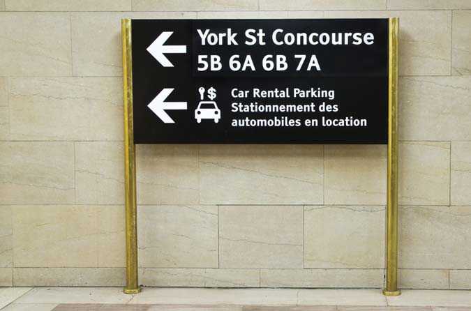 A sign at eye level. The sign is colour contrasted to the surrounding wall. Tiresias font is used in a colour that contrasts with the sign’s black background.
