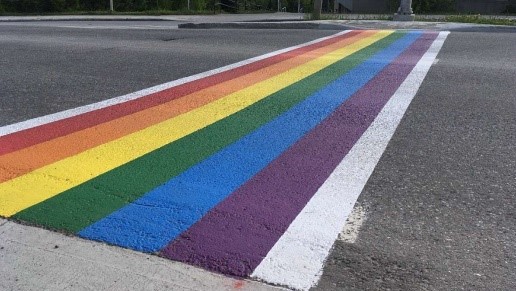 Traditional white crosswalk markings with parrallel rainbow-coloured strips extending fully from curb to curb.