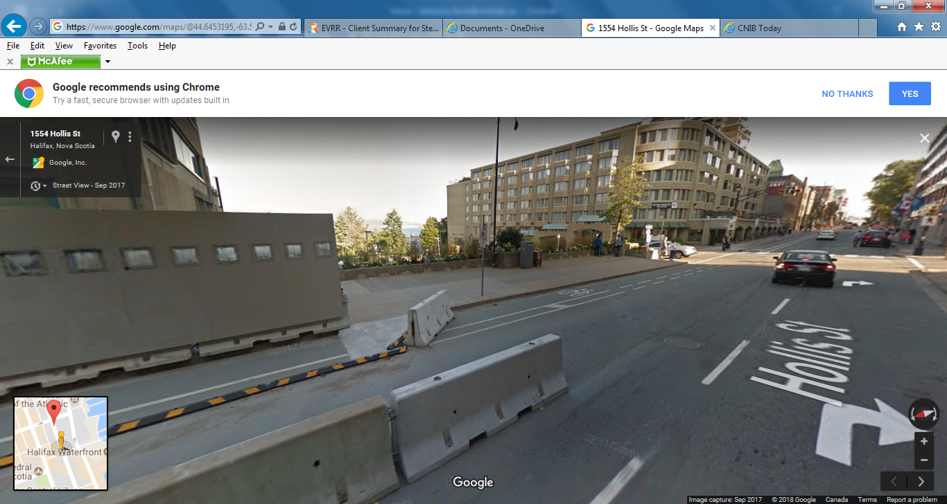 The temporary path of travel is separated from the construction by a hoarding, which is a non-permanent structure of solid construction, erected around the perimeter of a construction site. The path of travel is separated from traffic by a temporary concrete barrier.